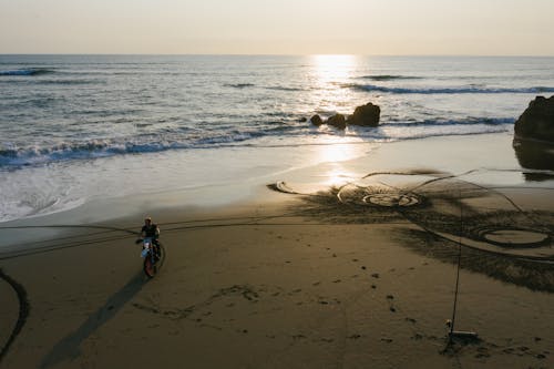 Unrecognizable biker riding on sandy beach in sunset