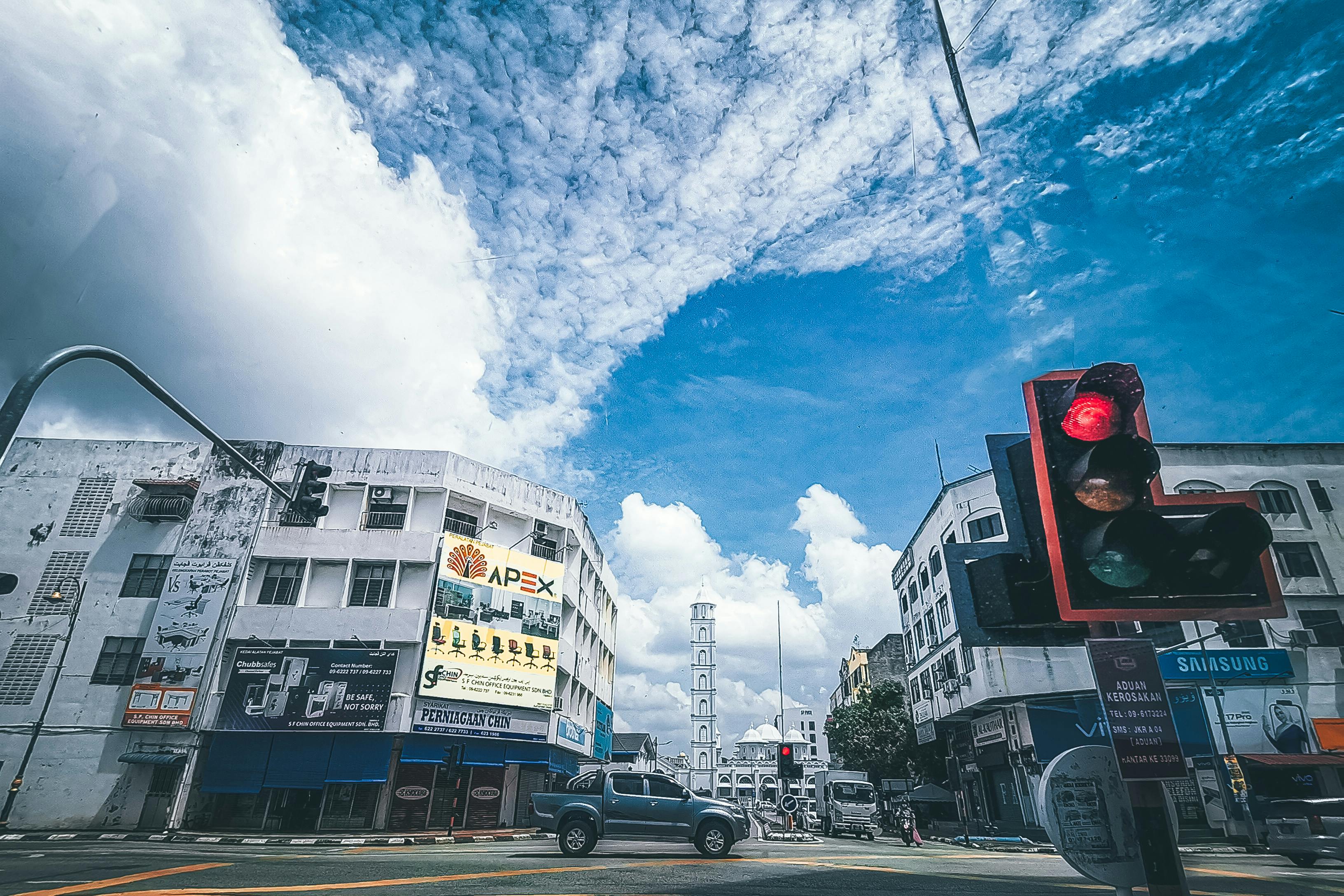 城市街景中，建筑物下可见多云蓝天，并配有红色红绿灯