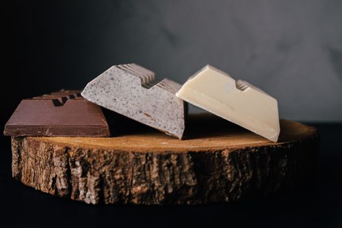 Free Assorted delicious sweet chocolate bars served on wooden tray against blurred gray background in studio Stock Photo