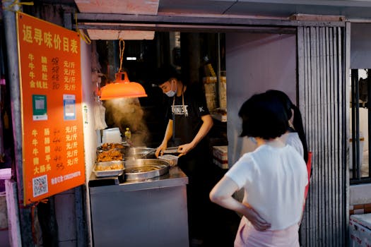 A street vendor prepares food at a night market stall while customers wait under dim lighting.