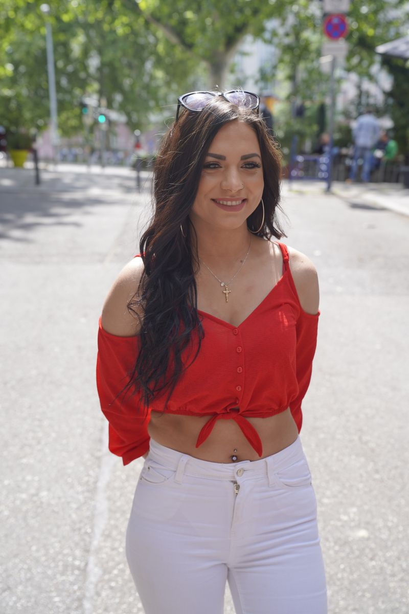 Smiling woman in red crop top and white jeans on sunny street