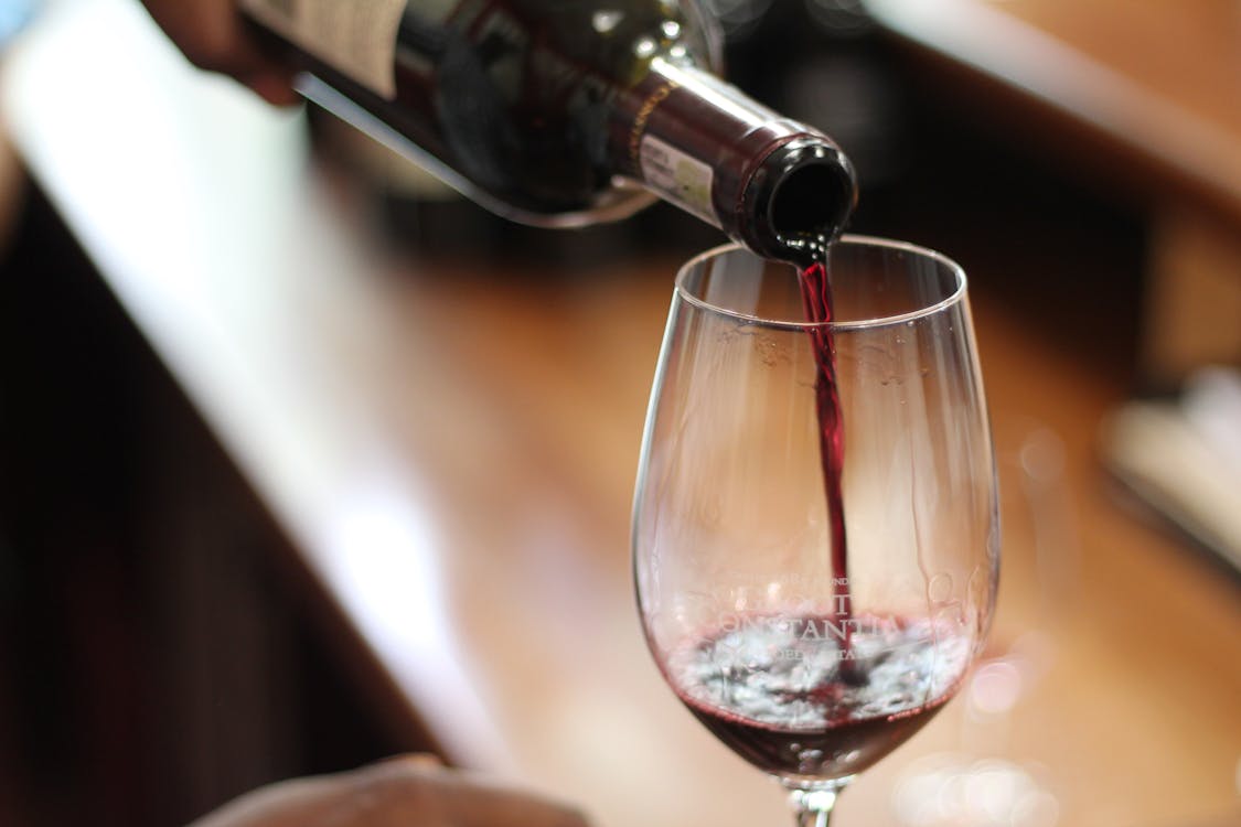 Person Pouring Red Wine into a Clear Wine Glass