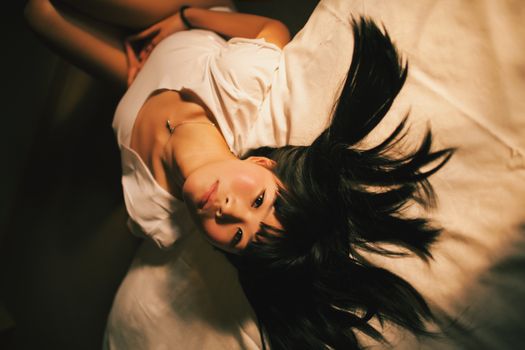 A young woman with long dark hair lies on a bed, captured in a cozy and intimate setting.