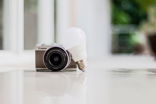 A Canon camera and LED light bulb on a glossy surface, symbolizing technology and innovation.