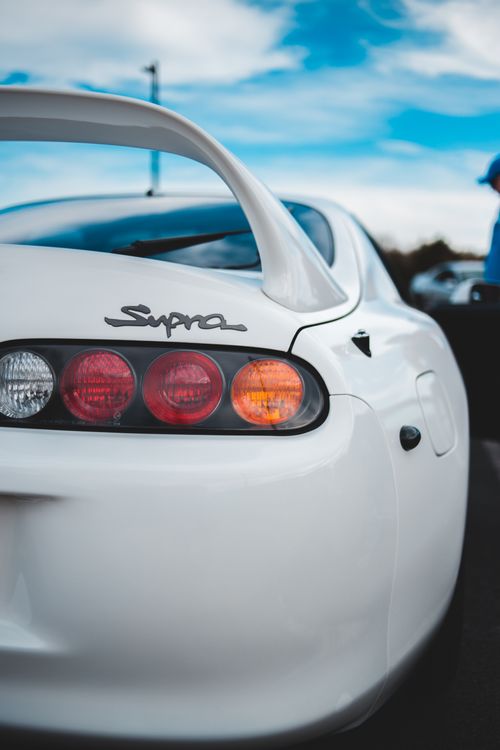 Free White sports car showcasing its rear design and distinctive wing spoiler, under a clear blue sky. Stock Photo