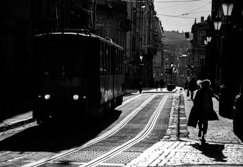 Grayscale Photo of People Walking on Sidewalk Near Train