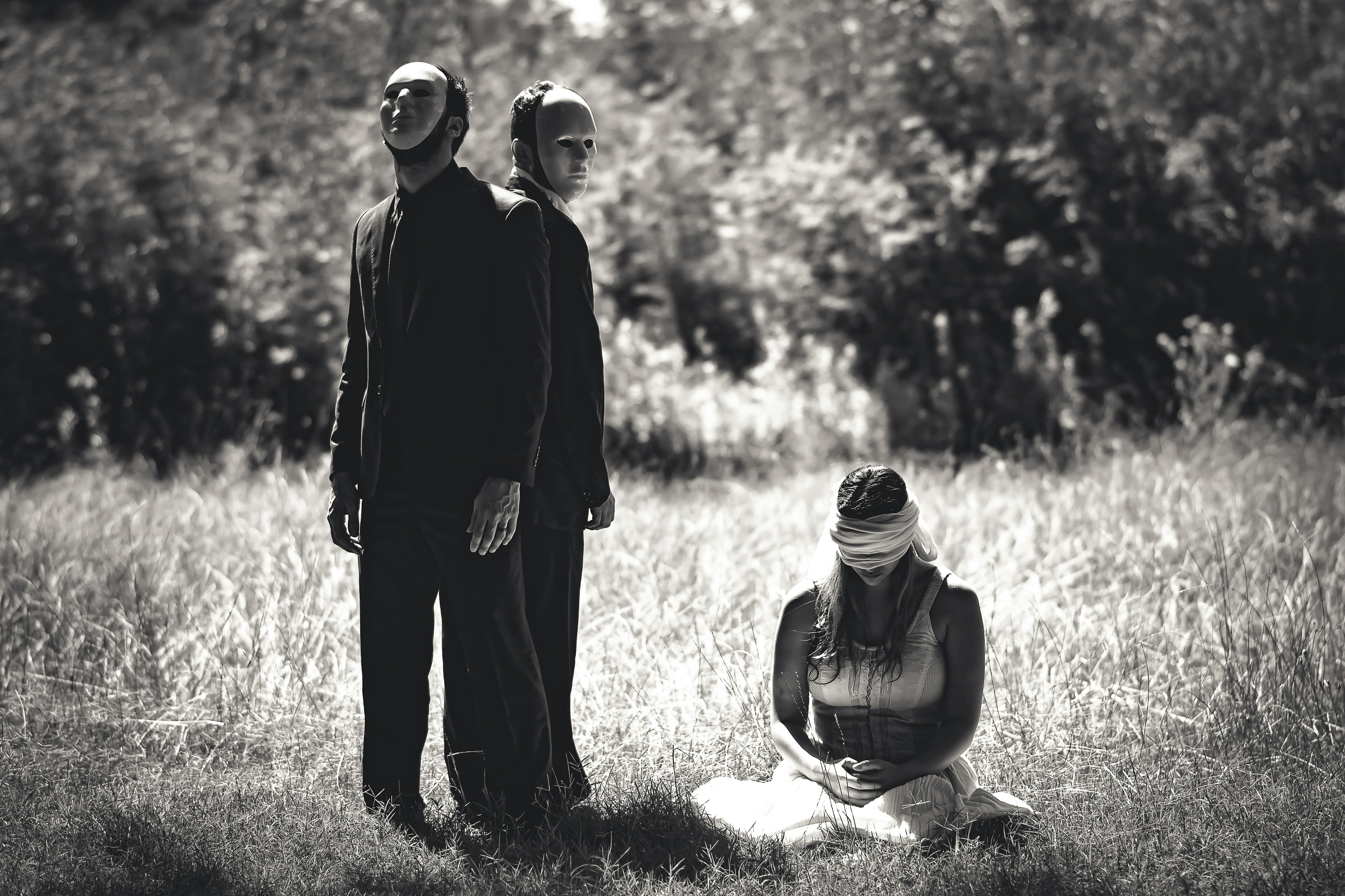 men in face masks standing over blindfolded woman