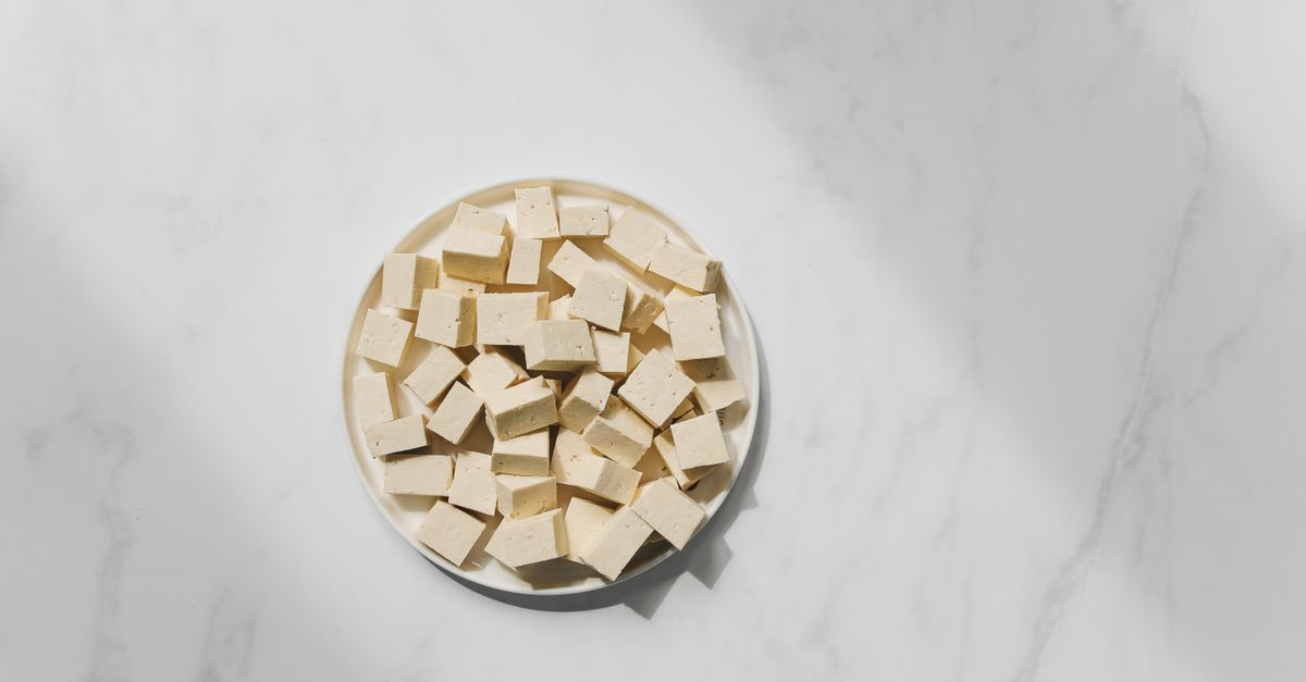 close-up of raw tofu cubes and dried yellow peas on a wooden cutting board, natural lighting