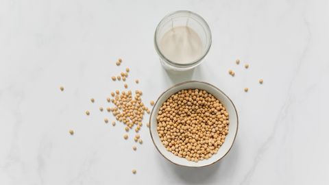 High-angle view of soybeans in a bowl and a glass of soy milk on a marble background.