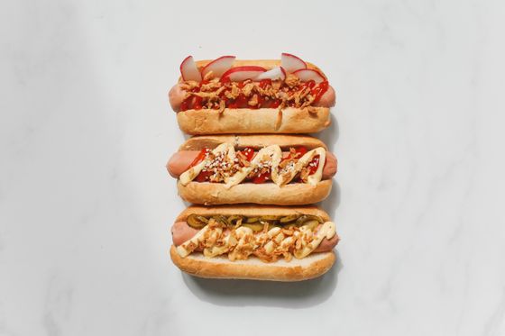Three loaded hot dogs topped with radish, crispy onions, pickles, sesame and creamy sauces