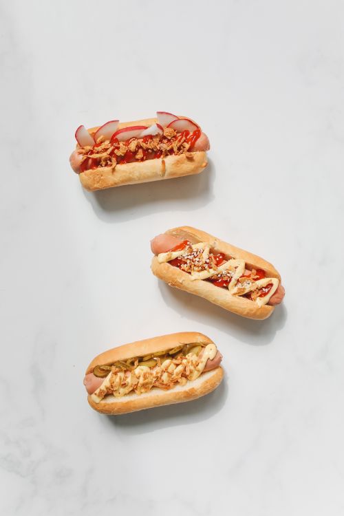 Free Three artisanal hot dogs with gourmet toppings on a white background. Perfect for food photography enthusiasts. Stock Photo