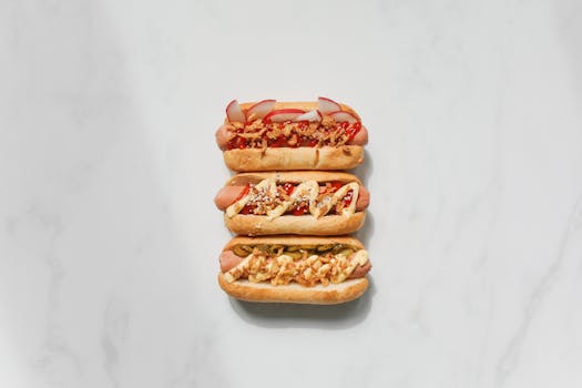 Three gourmet hot dogs with various toppings on a white surface.