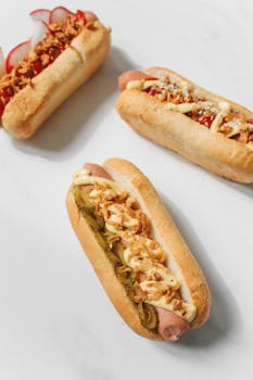Three gourmet hot dogs with various toppings on a white background.