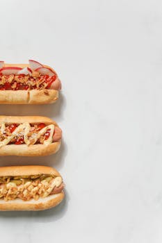 Three gourmet hot dogs topped with various ingredients on a white background, perfect for food photography.