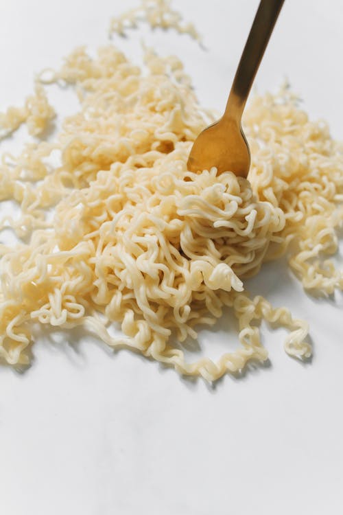 Noodles with Gold Fork on White Surface