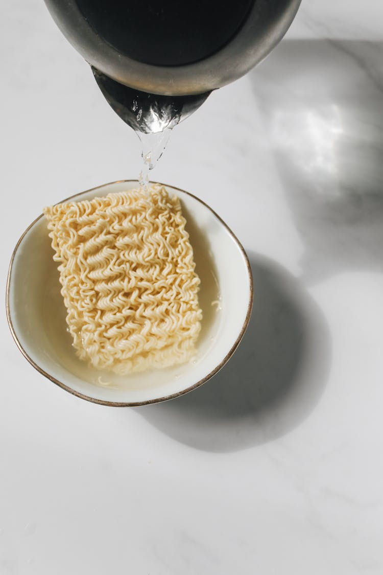 Photo Of Pitcher Pouring Hot Water On Bowl With Uncooked Noodles