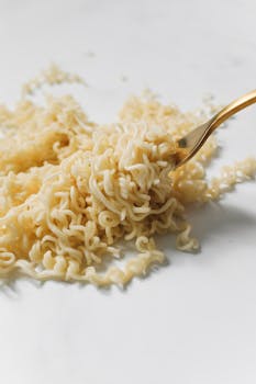 Close-up of instant noodles twirled on a golden fork on a white surface, highlighting texture and simplicity.