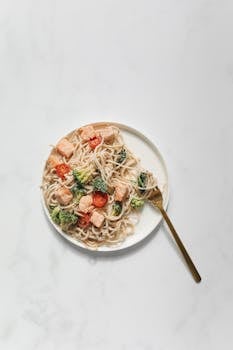 A plate of spaghetti topped with salmon and vegetables, perfect for a nutritious meal.