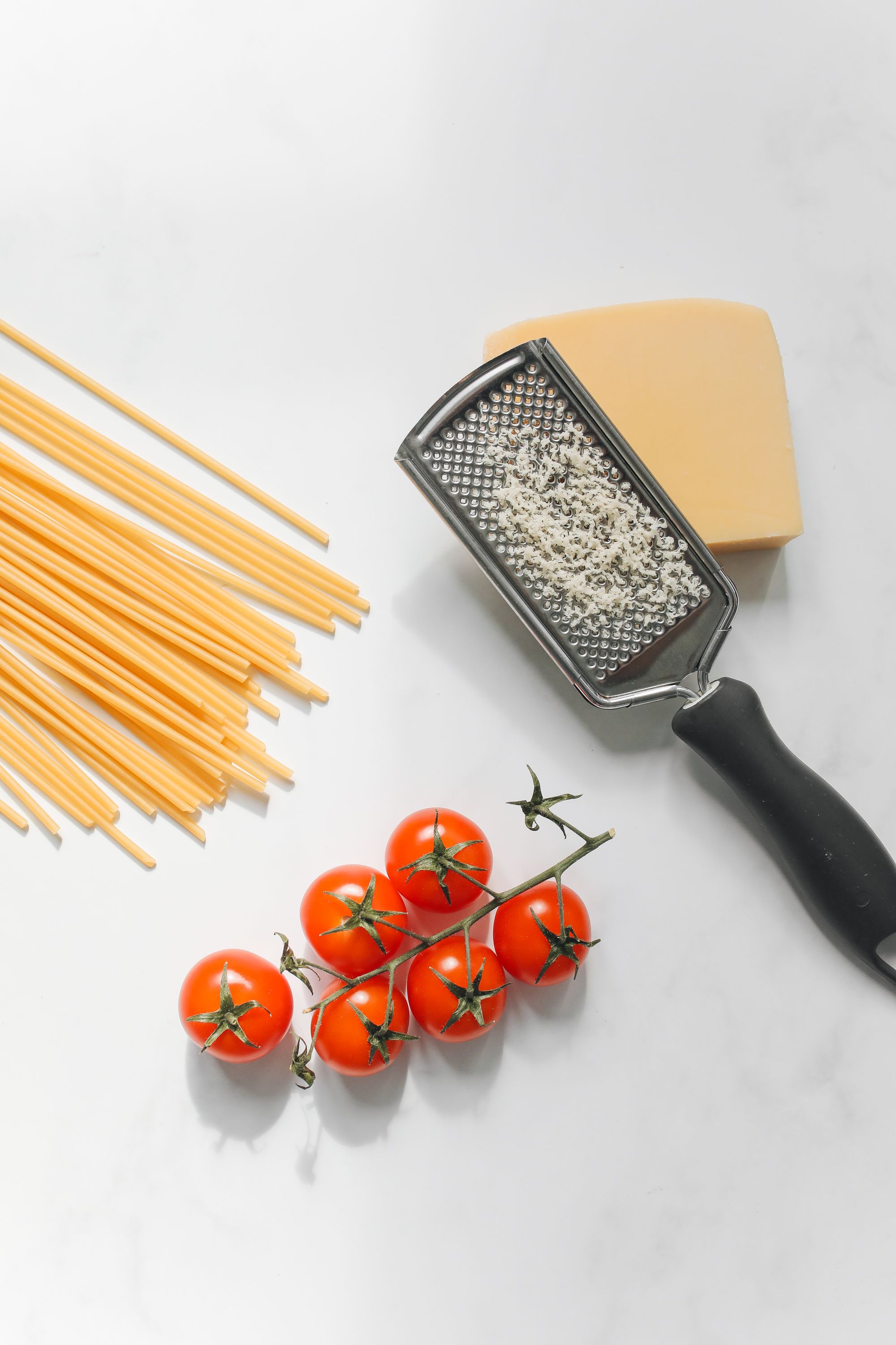 Box grater with grated cheese and tomatoes on white surface`