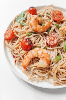 Appetizing shrimp spaghetti with cherry tomatoes served on a white plate.