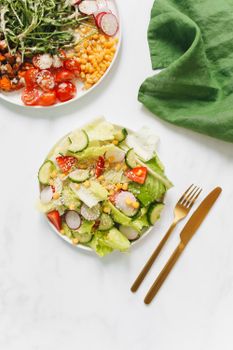 Healthy and colorful vegetarian salad with gold cutlery on white background, perfect for a nutritious meal.