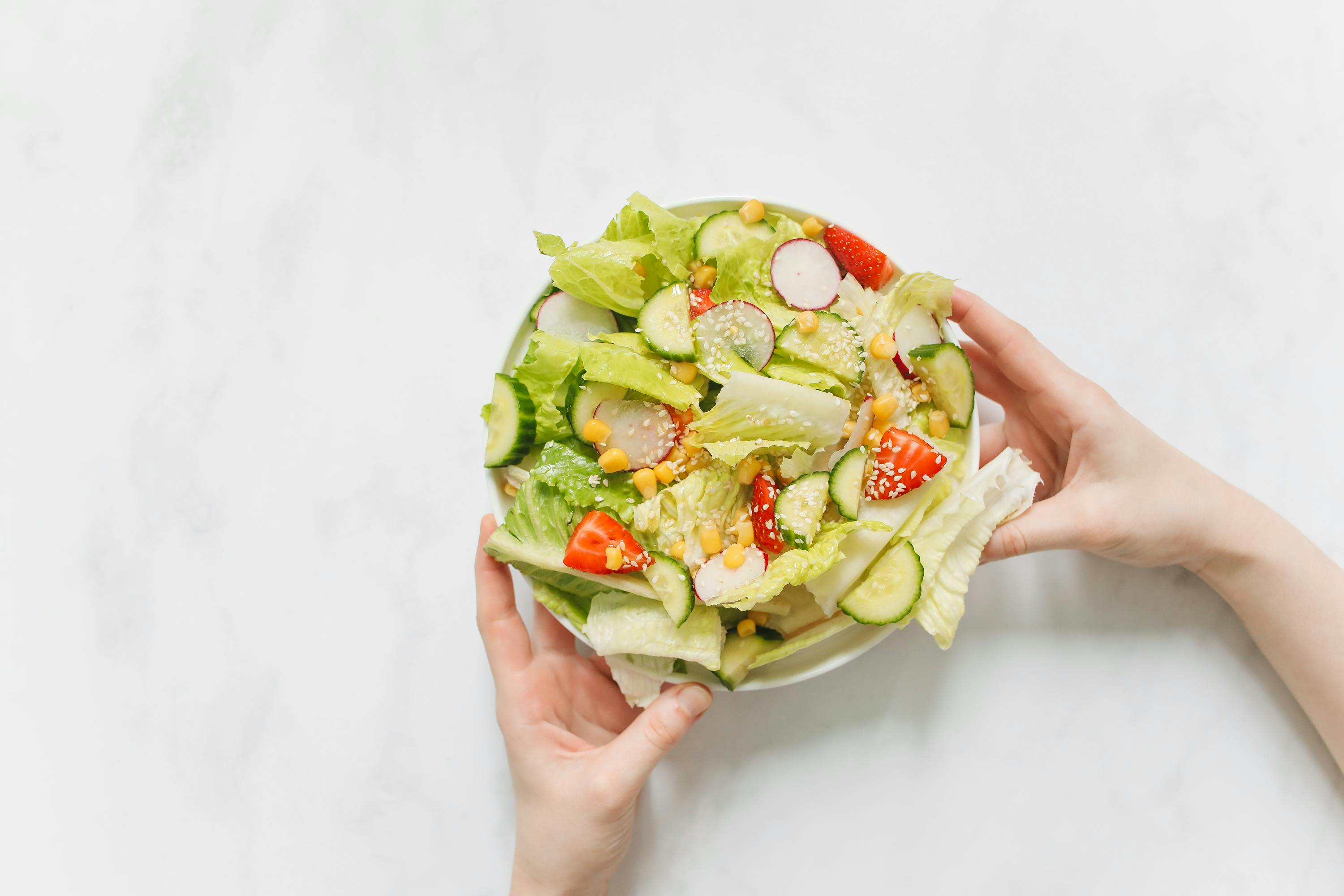 Hands holding a bowl of fresh vegetable salad with lettuce, cucumber, and radishes.
