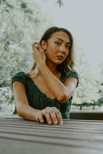 Low angle of ethnic woman touching hair while resting at wooden table in park