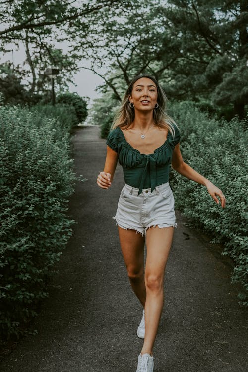 Free Positive Asian delight young female in casual outfit walking on pathway in green park Stock Photo