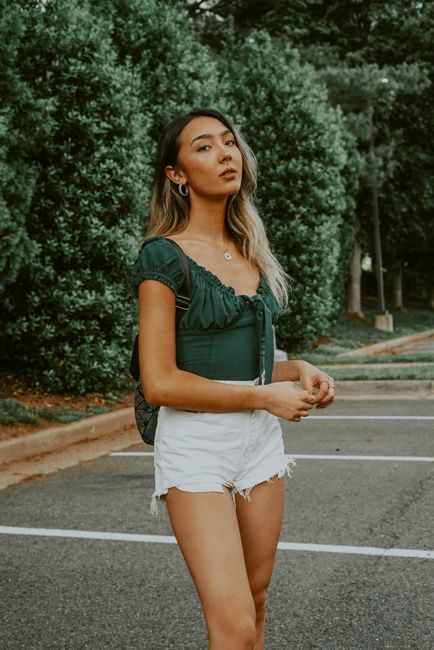 Dreamy Asian young woman in shorts and blouse standing alone against green trees