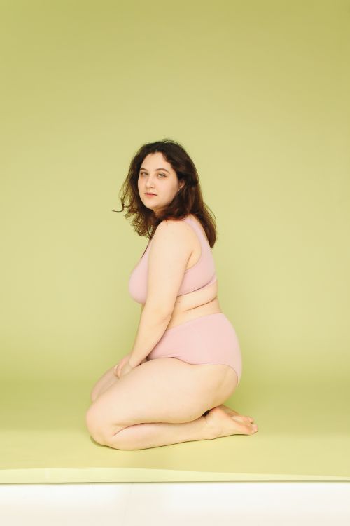 Free Woman in pink underwear posing confidently against a yellow background. Stock Photo
