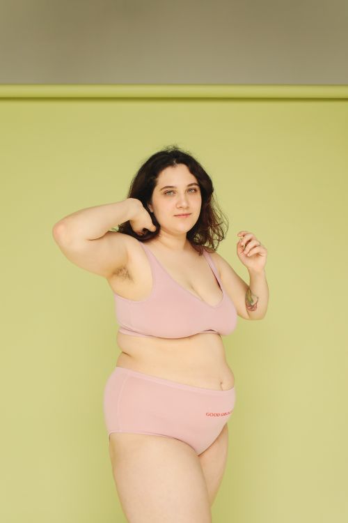 Free Curvy woman posing confidently in pink lingerie against a green studio background. Stock Photo