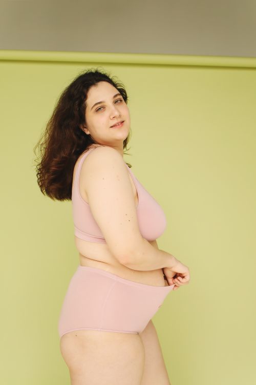 Free Confident plus size woman posing in pink underwear against a green background in a studio. Stock Photo