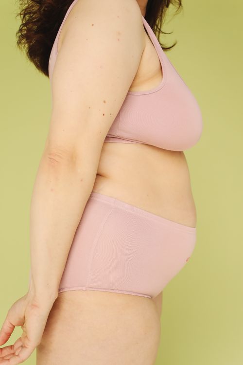 Free Side view of a plus-size woman in nude underwear against a green backdrop, promoting body positivity. Stock Photo