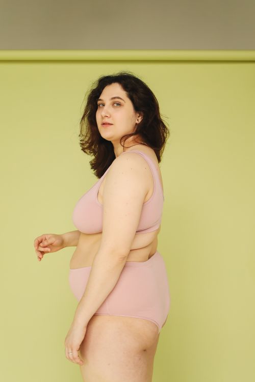 Free Portrait of a confident plus size woman in pink lingerie against a green background. Stock Photo