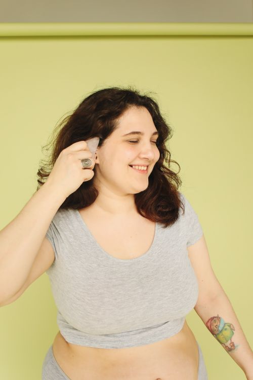 Free Smiling young woman in casual wear with vibrant tattoos poses against green backdrop. Stock Photo
