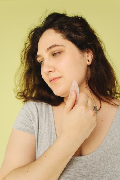 Free A woman performing a skincare routine using a gua sha stone on a green background. Stock Photo