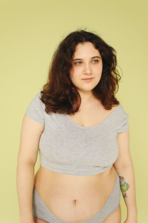 Free Confident woman embracing body positivity in a studio portrait with a green background. Stock Photo