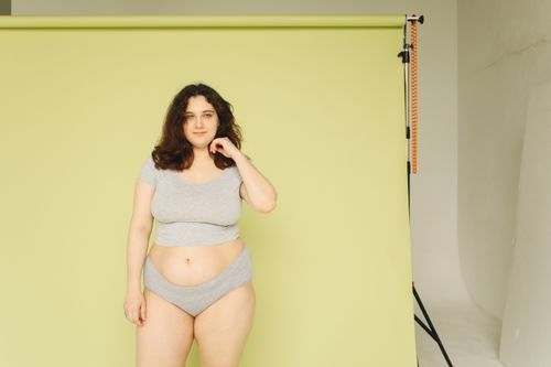 Free Portrait of a confident plus size woman in underwear against a yellow studio backdrop. Stock Photo