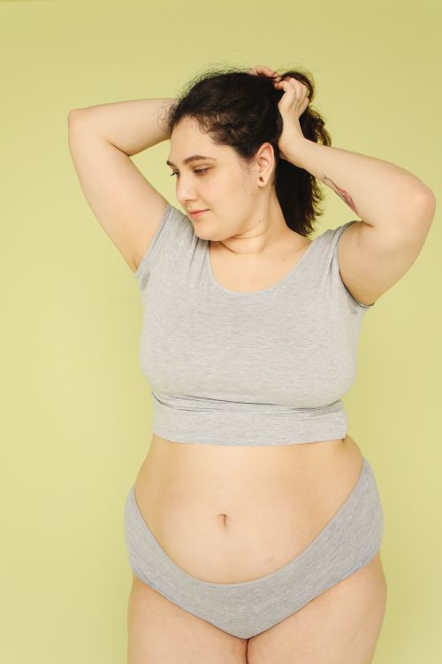Free Confident plus size woman in gray casual outfit poses against a yellow background in a studio setting. Stock Photo