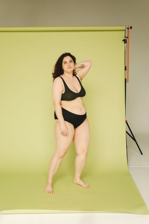 Free Plus size woman in black underwear posing confidently against a green backdrop in a studio. Stock Photo