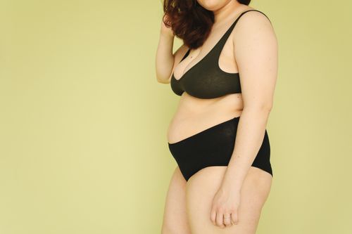 Free A plus-size woman in comfortable underwear against a soft yellow background, promoting body positivity. Stock Photo