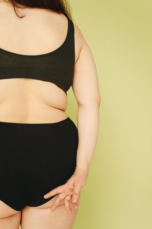 Free Back view of a confident plus size woman in black underwear on yellow background, promoting body positivity. Stock Photo