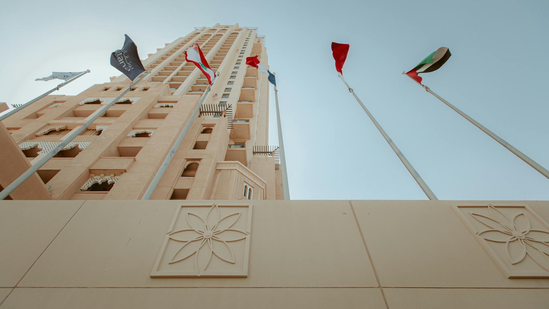 Low angle view of a modern building with flags in Dubai under a clear sky.