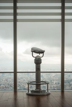 Modern stationary city binoculars near glass wall of high building to observe contemporary cityscape