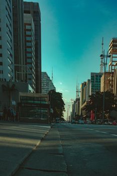 Low-angle view of a bustling city street lined with high-rise buildings under a clear sky.