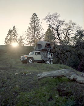 A rugged off-road vehicle with a rooftop tent set up in a forested area at sunset, perfect for an adventurous camping experience.