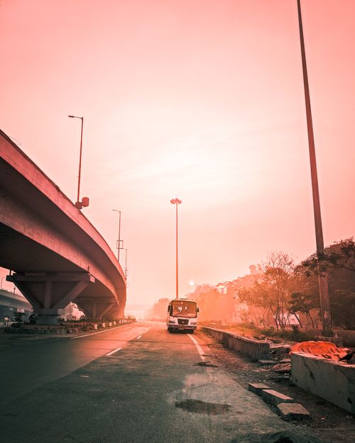 Free Perspective view of bus driving on empty roadway near cement bridge against cloudless sky during sunset time in summer on street Stock Photo