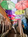 Multicolored umbrellas hanging in air in narrow alley of old street with memorial on wall during daytime in city outside