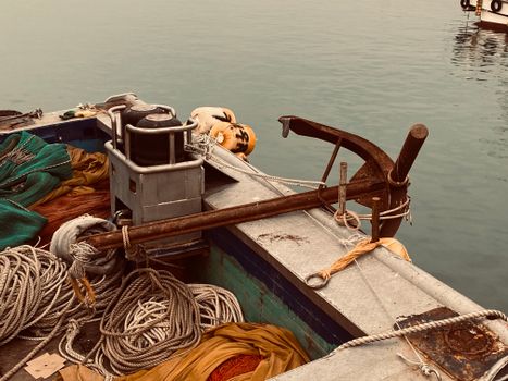 Metal fish boat with ropes and hanging anchor moored in harbor with calm water during daytime in coastal city outside
