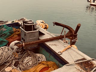 Metal fish boat with ropes and hanging anchor moored in harbor with calm water during daytime in coastal city outside